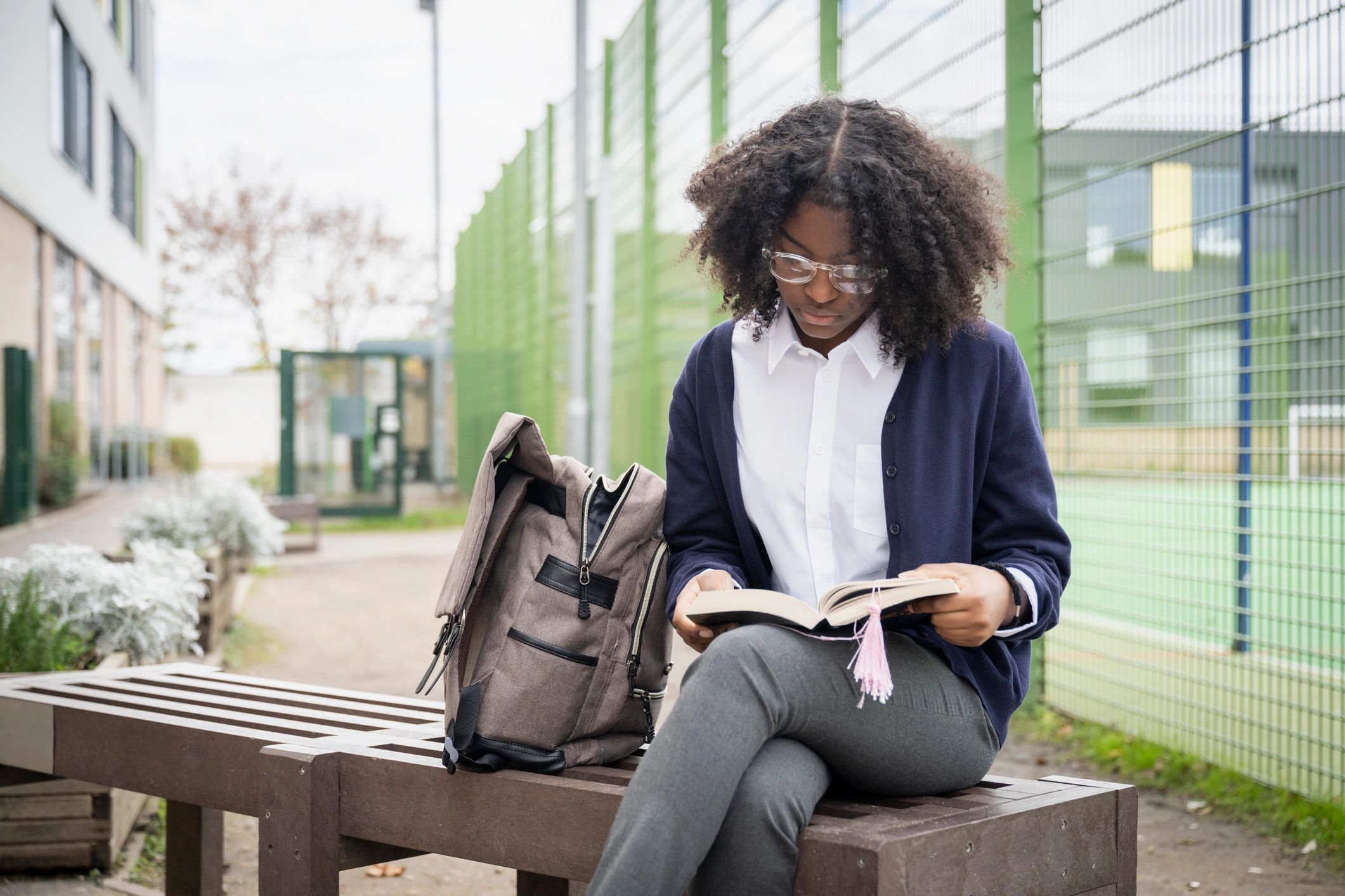 Student reading a book outdoors with backpack nearby