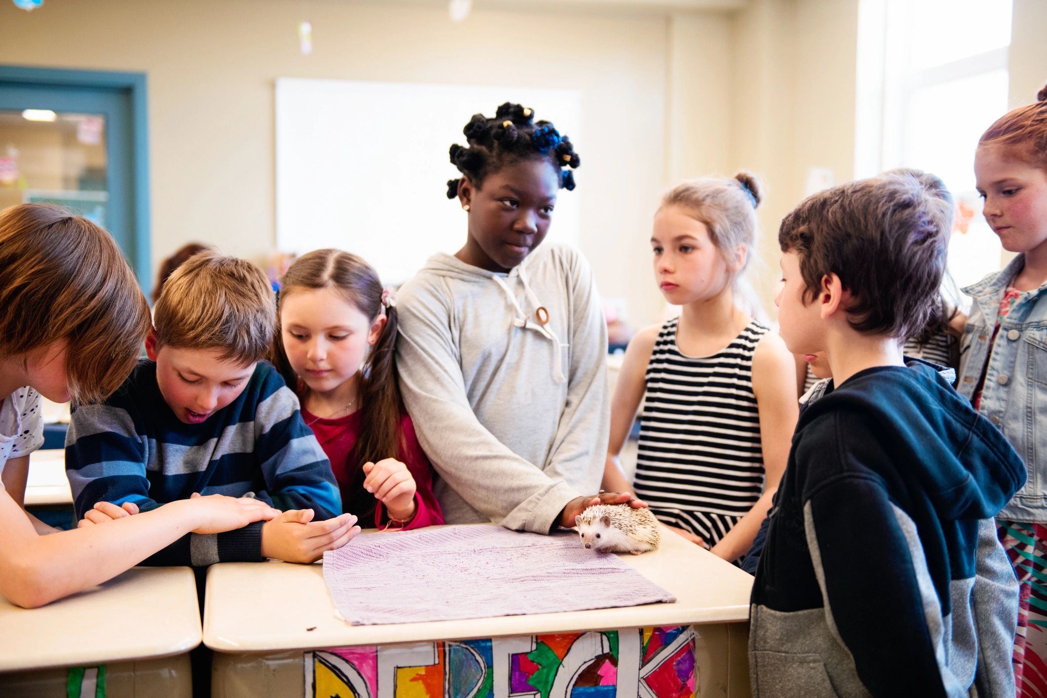 Upper elementary students gathered around a classroom desk during a presentation